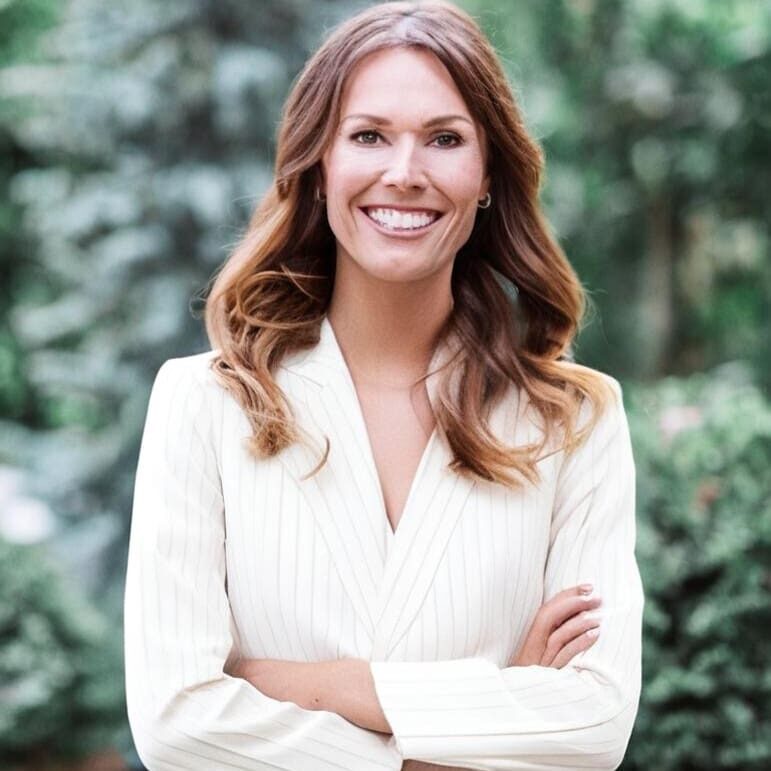 Smiling woman with crossed arms outdoors in a white sweater.